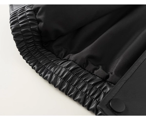 Detail of black leather jacket elastic hem and matte metal snap button with fine stitching