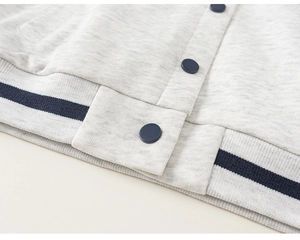 Close-up of contrast rib-knit hem and dark blue buttons on grey kids varsity jacket