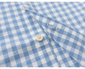 Detail of blue gingham cotton shirt fabric featuring a white four-hole button and stitching