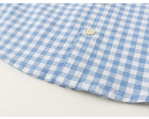 Detailed close-up of blue gingham shirt weave with beige buttons and curved hem stitching