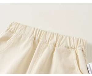 Detailed macro view of the elastic waistband and pocket on cream cotton trousers