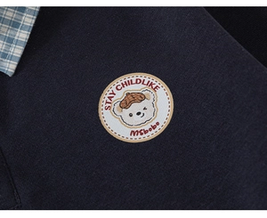 Détail du sweat-shirt bleu marine montrant le col à carreaux et la broderie ours