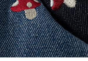 Dettaglio del tessuto denim blu scuro con ricamo a forma di fungo rosso sui pantaloni