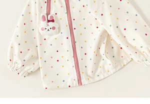 Close-up of cream children's jacket featuring colorful polka dots and a cute rabbit patch