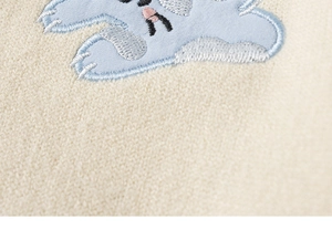 Detail van een crème gebreide trui met lichtblauwe dierenborduring en zachte textuur