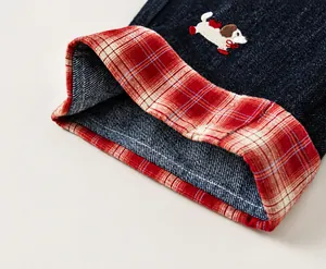 Detail of dark blue denim cuff featuring cartoon dog embroidery and red tartan lining