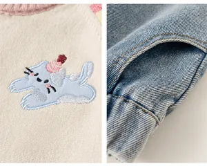 Detail van kattenborduurwerk op gebreid vest en zijzakken van de spijkerbroek voor kids