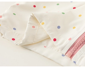 Detail shot of colorful polka dots on off-white kids jacket with pink resin zipper