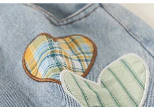Detail of light blue denim pants with yellow and green heart-shaped embroidery patches