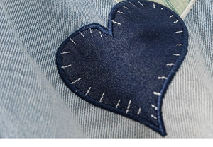 Detail of dark blue heart patch embroidery on light blue denim fabric for girls' jeans
