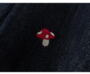 Close-up of high-quality navy denim fabric with detailed red mushroom embroidery
