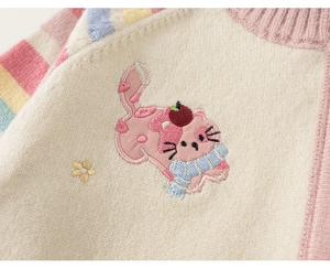 Detail van gebreide trui met regenboogmouw en roze geborduurde kattenpatroon details
