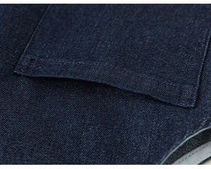 Détail du tissu denim bleu foncé avec coutures renforcées sur la poche du gilet pour enfant