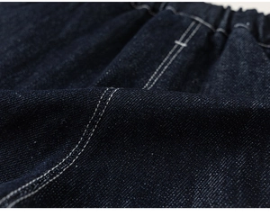 Close-up of dark blue denim texture with white contrast stitching and elastic waistband