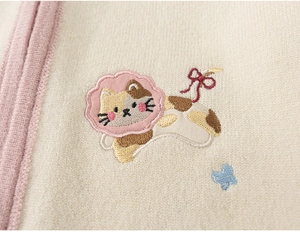 Detail van geborduurde lapjeskat en vlinder op een beige gebreid kindervestje