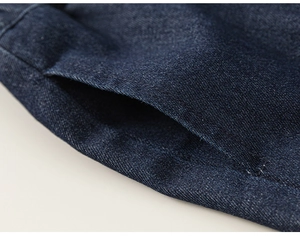 Gros plan détaillé sur la texture du denim bleu foncé et les coutures de ce jean enfant