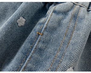 Detail van blauwe denimstof met witte bloemborduring en gele contrasterende stiksels
