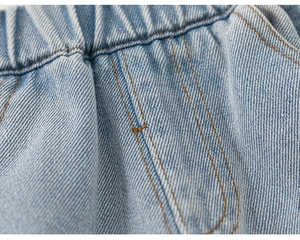 Detail of girls' blue denim pants showing elastic waistband and yellow contrast stitching