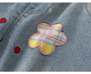 Detail van bloemborduursel en twill-textuur op een blauw denim vest voor meisjes