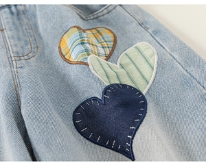Detail of girls' blue jeans with heart-shaped patchwork in plaid and striped fabrics