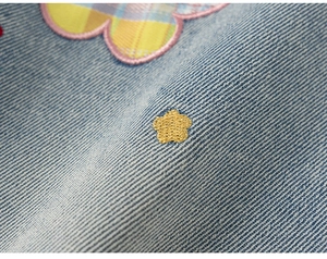 Macro detail van lichtblauwe denim stof met kleurrijke bloemenborduring en gele ster detail