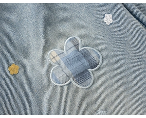 Detail van lichtblauwe denim met bloemenpatchwork en kleurrijk borduurwerk