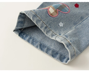 Detail van blauwe denimstof met hart-patchwork en bloemenborduursel op kinderkleding