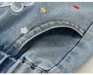 Detalle de mezclilla azul claro con bordado floral y costuras amarillas en contraste para niña