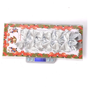 Detailed view of six silver Christmas bows on card packaging being weighed at 17.0g