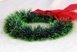 Detail of green tinsel Christmas wreath with a large red velvet bow on a soft warm background