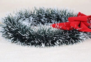 Detail of green Christmas wreath with frosted tips and a red fabric bow on a soft rug