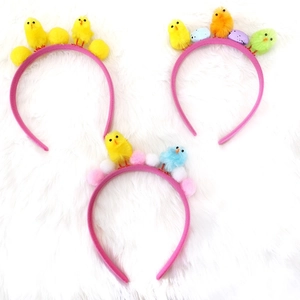Tre cerchietti pasquali con pulcini di peluche e uova colorate su morbido tessuto rosa
