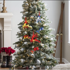 Close-up of three festive glitter reindeer ornaments with bells hanging on a snowy Christmas tree