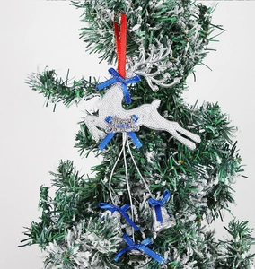 Silver sequin reindeer ornament with blue bow and bells on a snowy Christmas tree