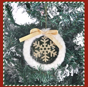 Close-up of white woven wreath with gold glitter snowflake and beige bow on a tree