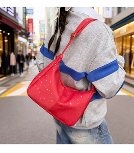Sac hobo rouge à motif d'étoiles argentées porté par un mannequin dans une rue urbaine