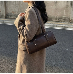 Détail du sac polochon en cuir marron foncé porté avec un manteau en laine élégant