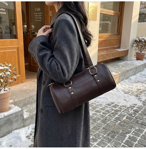 Détail d'un sac oreiller en cuir marron foncé avec clous argentés porté par un modèle