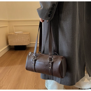 Détail du sac Boston vintage en cuir café avec rivets argentés porté à l'épaule par le mannequin