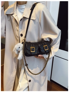 Close-up of black leather dumpling bag featuring metal buckles and a plush rabbit charm