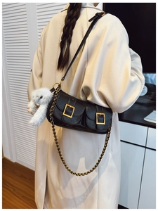 Detail of black faux leather baguette bag with gold buckles and plush charm on white coat