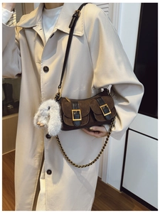 Detail of dark brown dumpling bag with suede texture, gold buckles, and plush rabbit charm