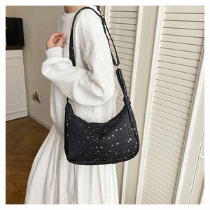 Détail d'un sac bandoulière noir avec motifs étoiles et pois porté dans un décor maison