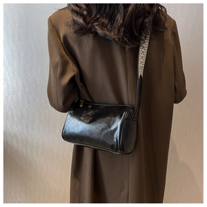 Sac cylindre en cuir noir brillant avec texture et bandoulière tissée sur modèle