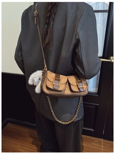 Brown suede dumpling bag worn with metal chain, vintage buckle and plush doll detail