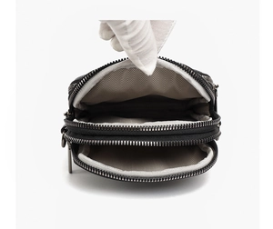Close-up of black leather crossbody bag with multiple zippers and wavy pattern lining