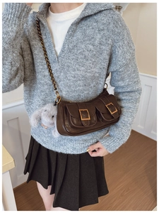 Detail of dark brown leather baguette bag with dual flap pockets and plush rabbit charm