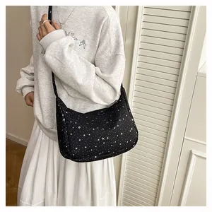 Détail d'un sac bandoulière noir en demi-lune avec motif étoiles sur une tenue de sweat à capuche