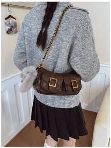 Deep brown leather dumpling bag styled with chain strap and plush pendant on model