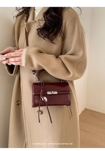 Detail of dark red glossy leather crossbody bag with silver rotating clasp and tassel accent